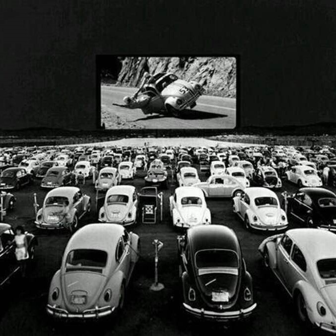 VW bug owners watching a 'Herbie' movie at a 1960s drive-in theater