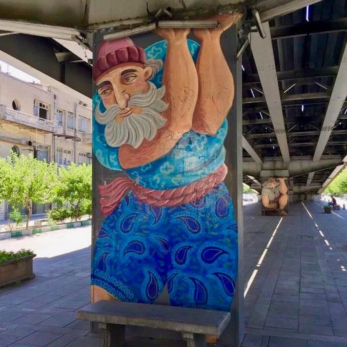 Traditional strongmen ('pahlavans') are shown holding up elevated roadways in these Tehran murals