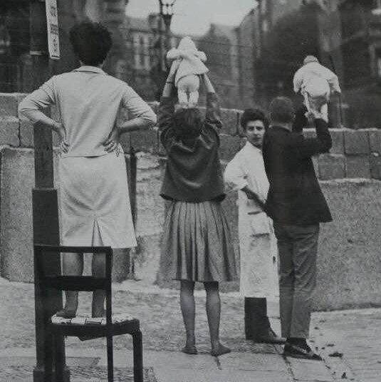 Children being shown to their grandparents, over a section of the Berlin Wall