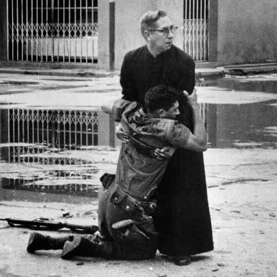 Priest holding a dying soldier, as bullets fly around them, Venezuela, 1962