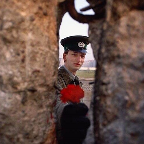 An East German border guard offering a flower through a gap in the Berlin Wall on the morning it fell, 1989