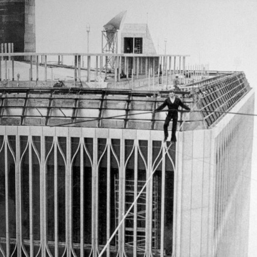 Man waling on a tightrope between the tops of NYC's Twin Towers