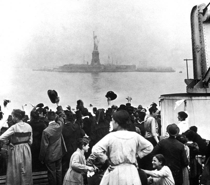 A group of immigrants traveling aboard a ship celebrate as they catch their first glimpse of the Statue of Liberty, 1910