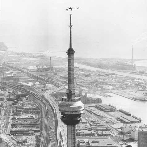 A helicopter installs a section of antenna mast of the CN Tower in Toronto, Canada, 1975