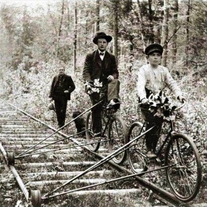 A father and son ride bicycles outfitted to move on train tracks in Pelston, Michigan, circa 1910