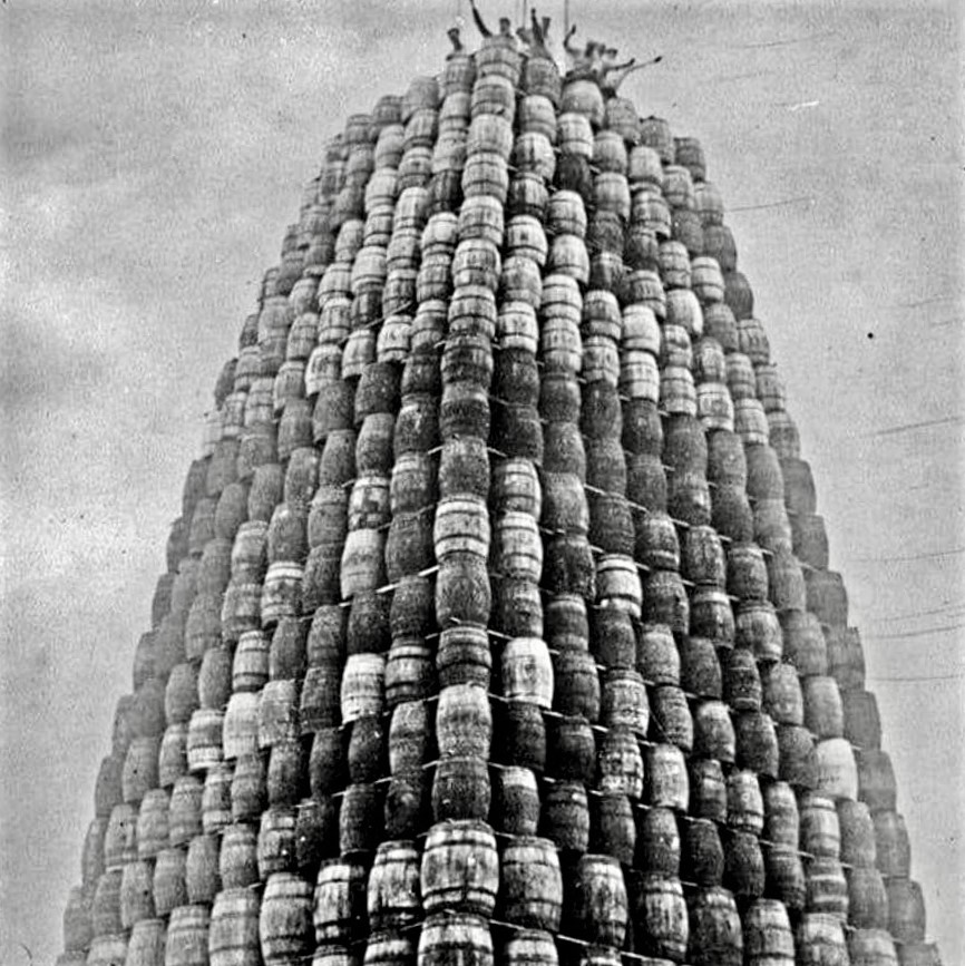 Workers wave from the top of a tower built from confiscated barrels of alcohol, being prepared for burning during the Prohibition, 1929